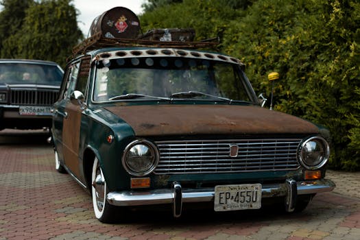 Front view of a rusty vintage car parked outdoors with lush greenery.