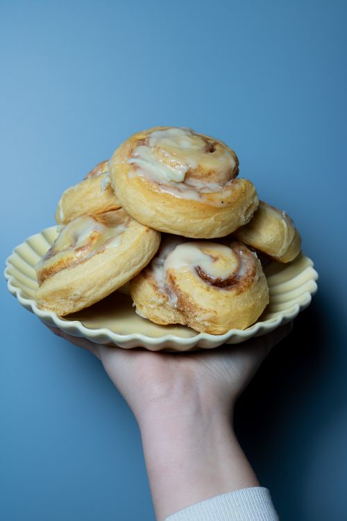 Free Close-up of freshly baked cinnamon rolls on a plate held by a hand against a blue background. Stock Photo
