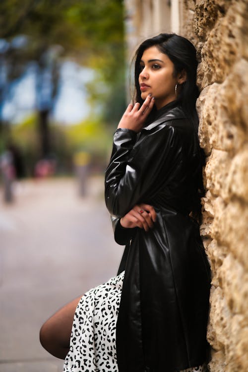 A Woman in Black Leather Jacket Leaning on Concrete Wall