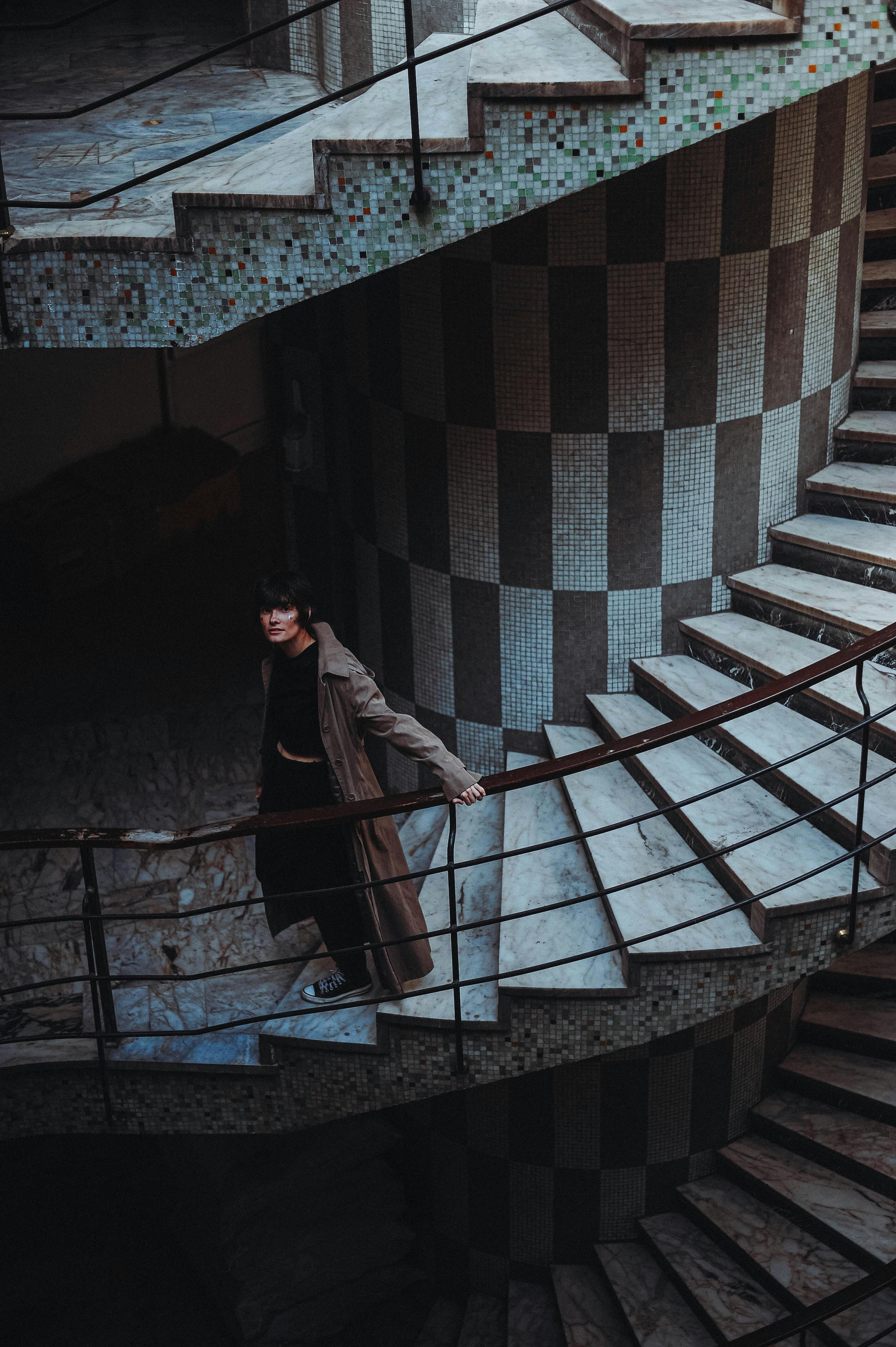 A woman descends a dimly lit spiral staircase with checkered walls indoors.