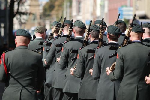 Free A group of soldiers in uniforms holding firearms, marching through a street in an outdoor formation. Stock Photo