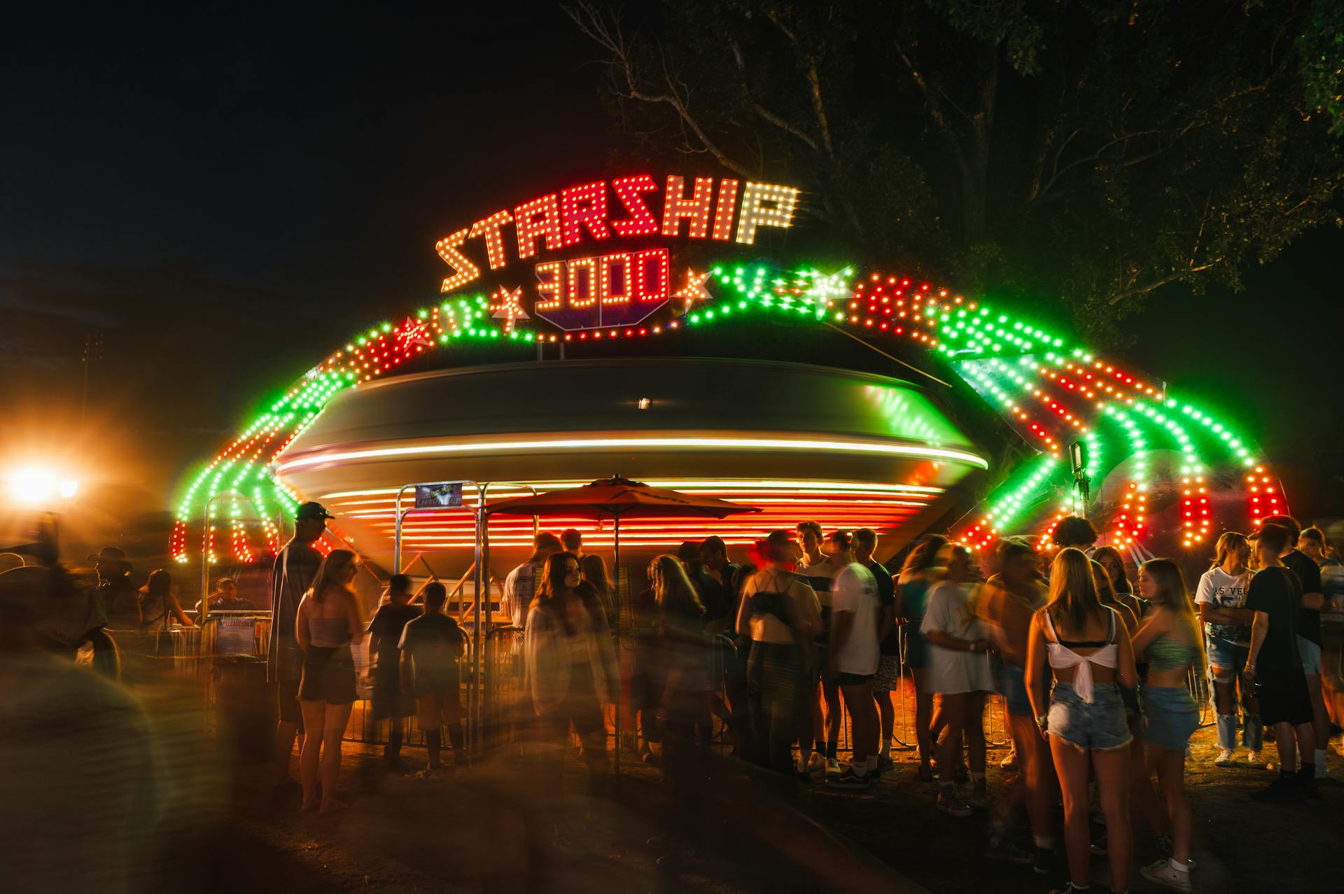 Blurred crowd enjoying the Starship 3000 ride at night with vibrant neon lights.