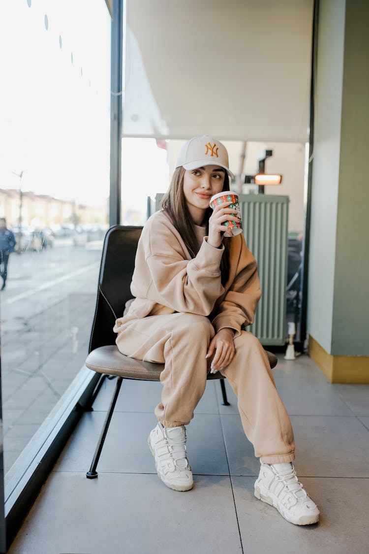 Woman In Sportswear Sitting On Chair Drinking Takeaway Coffee