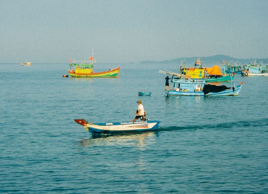 Traditional fishing boats sail on the calm sea near Phu Quoc, Vietnam, under a clear sky.