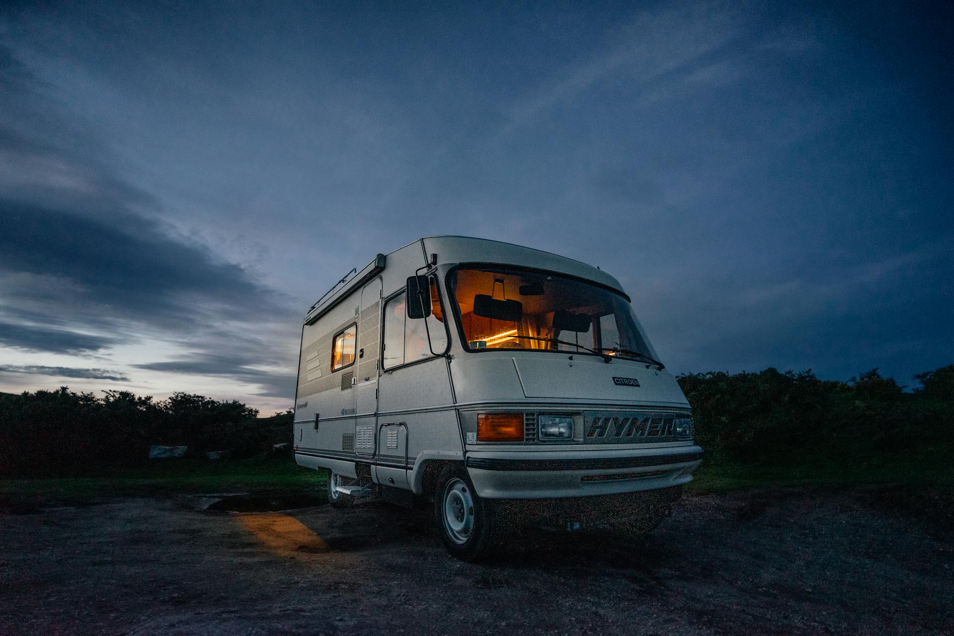 Camper van parked in rural area at twilight, glowing warmly inside, perfect for vanlife enthusiasts.