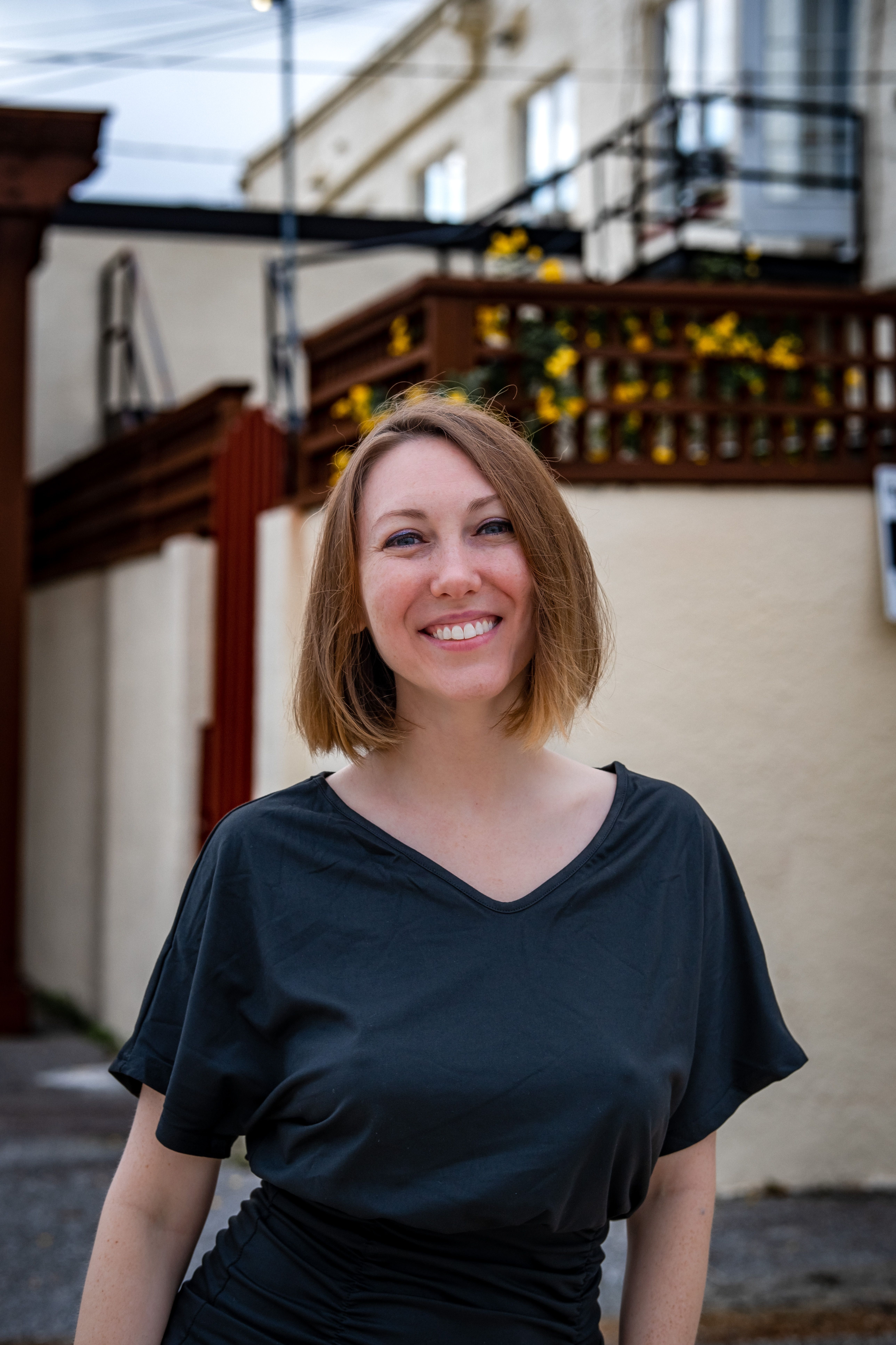 A cheerful woman with short hair smiles outdoors, showcasing a casual urban moment.