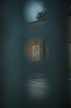 Eerie view of an old building through a blurred fence, creating a mysterious atmosphere.