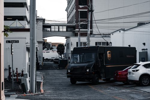 Free A UPS truck parked in an urban alleyway surrounded by buildings and parked cars. Stock Photo