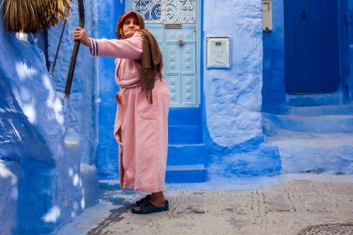 Free Elderly woman in pink robe stands in the iconic blue alley of Chefchaouen, Morocco. Stock Photo