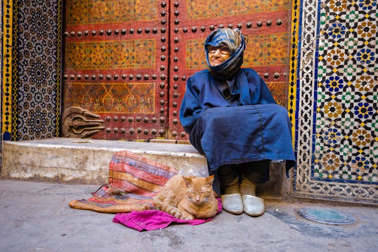 Elderly Woman With A Cat Sitting On The Street