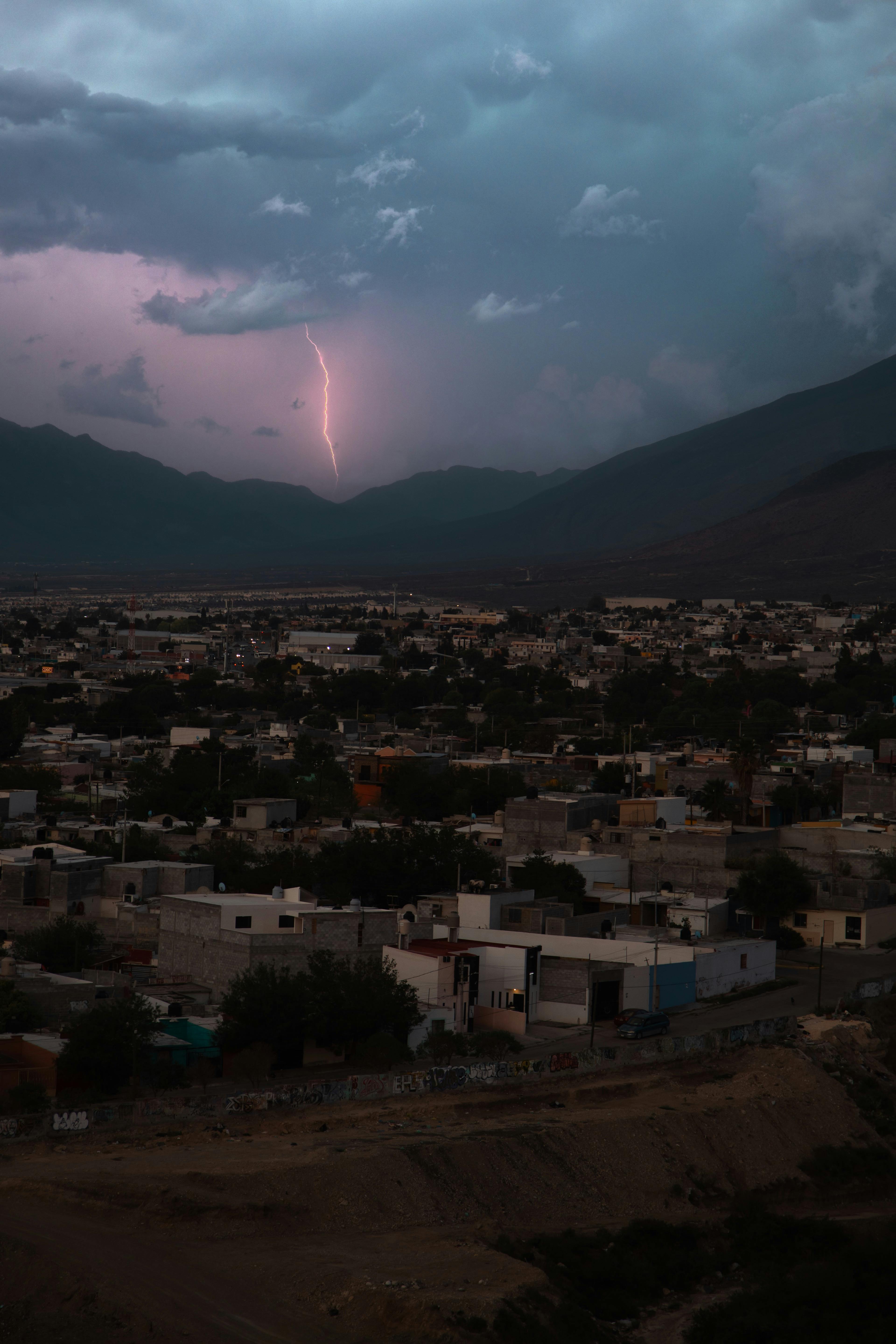 A striking lightning bolt illuminates a town nestled in mountainous terrain under a stormy sky.