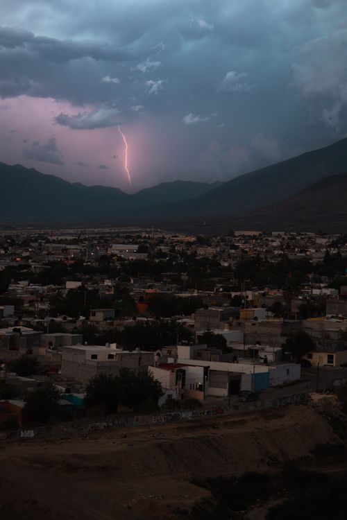 Free A striking lightning bolt illuminates a town nestled in mountainous terrain under a stormy sky. Stock Photo