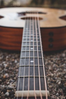 Detailed close-up of an acoustic guitar on gravel background, highlighting the strings and neck.