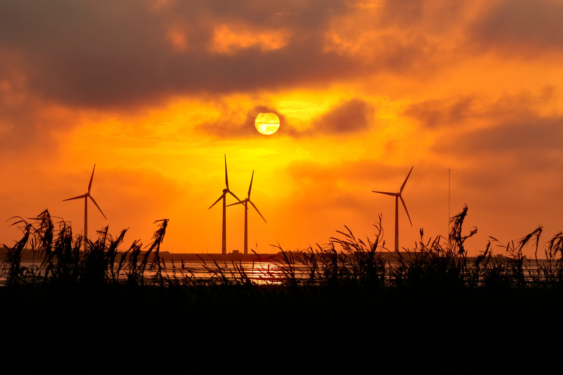 Silhouetted wind turbines under a vivid orange sky during sunset, symbolizing renewable energy.