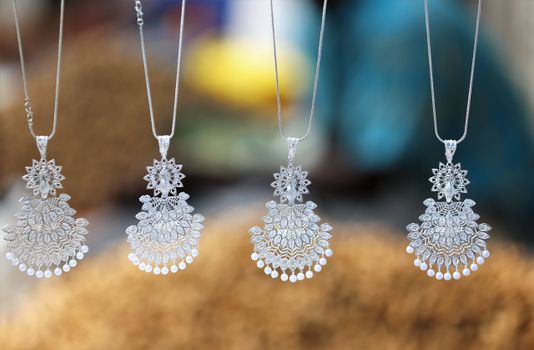 Close-up of beautiful silver necklaces with intricate designs hanging with a blurred background.