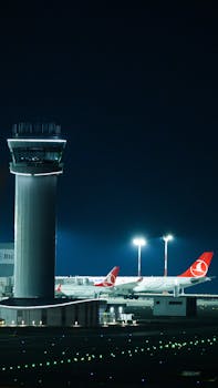 Illuminated control tower and Turkish Airlines planes at Istanbul Airport during nighttime.