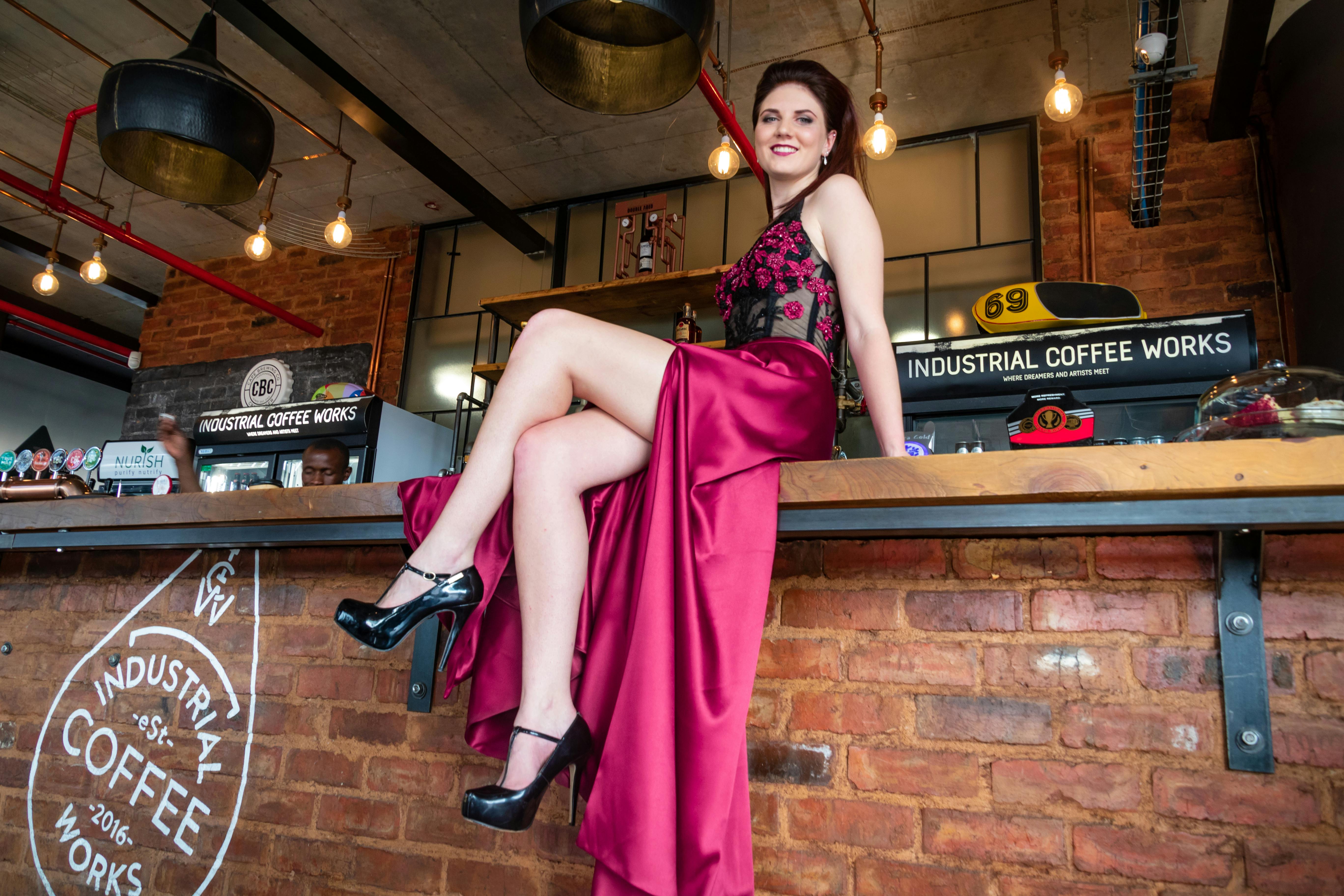 Elegant woman in a red dress sitting at a vintage-style coffee shop counter.