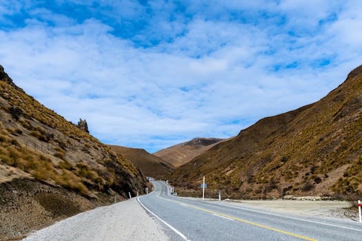 Peaceful curvy road through brown mountains under blue sky in New Zealand.