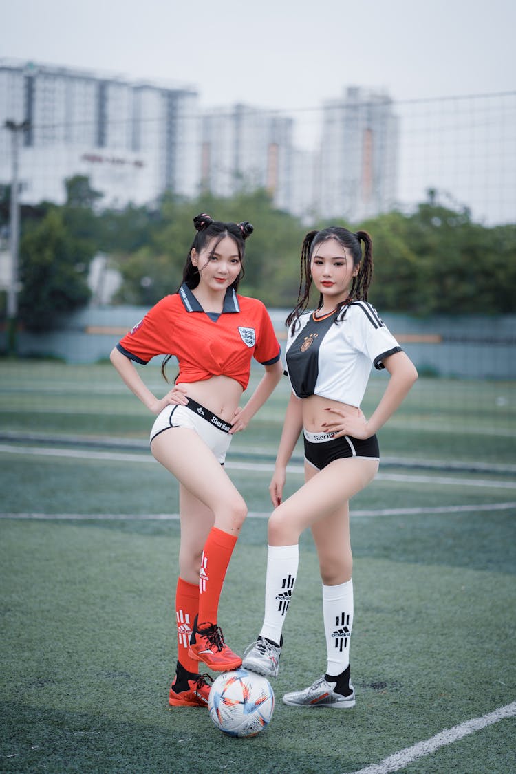 Young Women In Soccer Jerseys Stepping On A Football