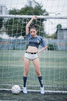 Model posing in sporty attire on a soccer field with ball and goal post.