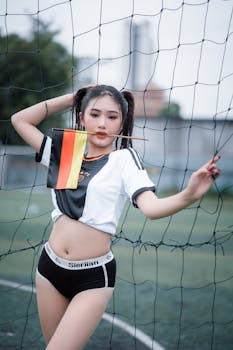 A young woman in sports attire holds a Germany flag on a soccer field, showcasing athleticism and national pride.