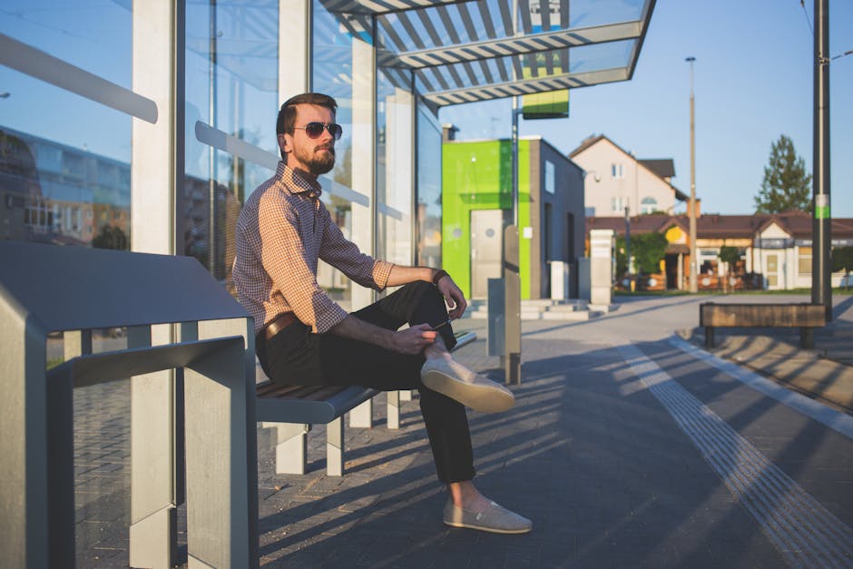 Man Wearing Sunglasses Sitting at Bus Stop during Daytime Man Wearing Sunglasses Sitting at Bus Stop during Daytime