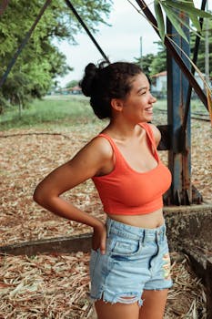 Smiling woman in denim shorts and orange top outdoors in Codó, MA, Brazil.