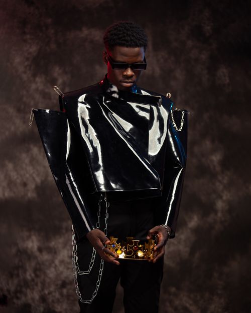 Free Stylish portrait of a man in avant-garde attire holding a crown against a textured backdrop. Stock Photo