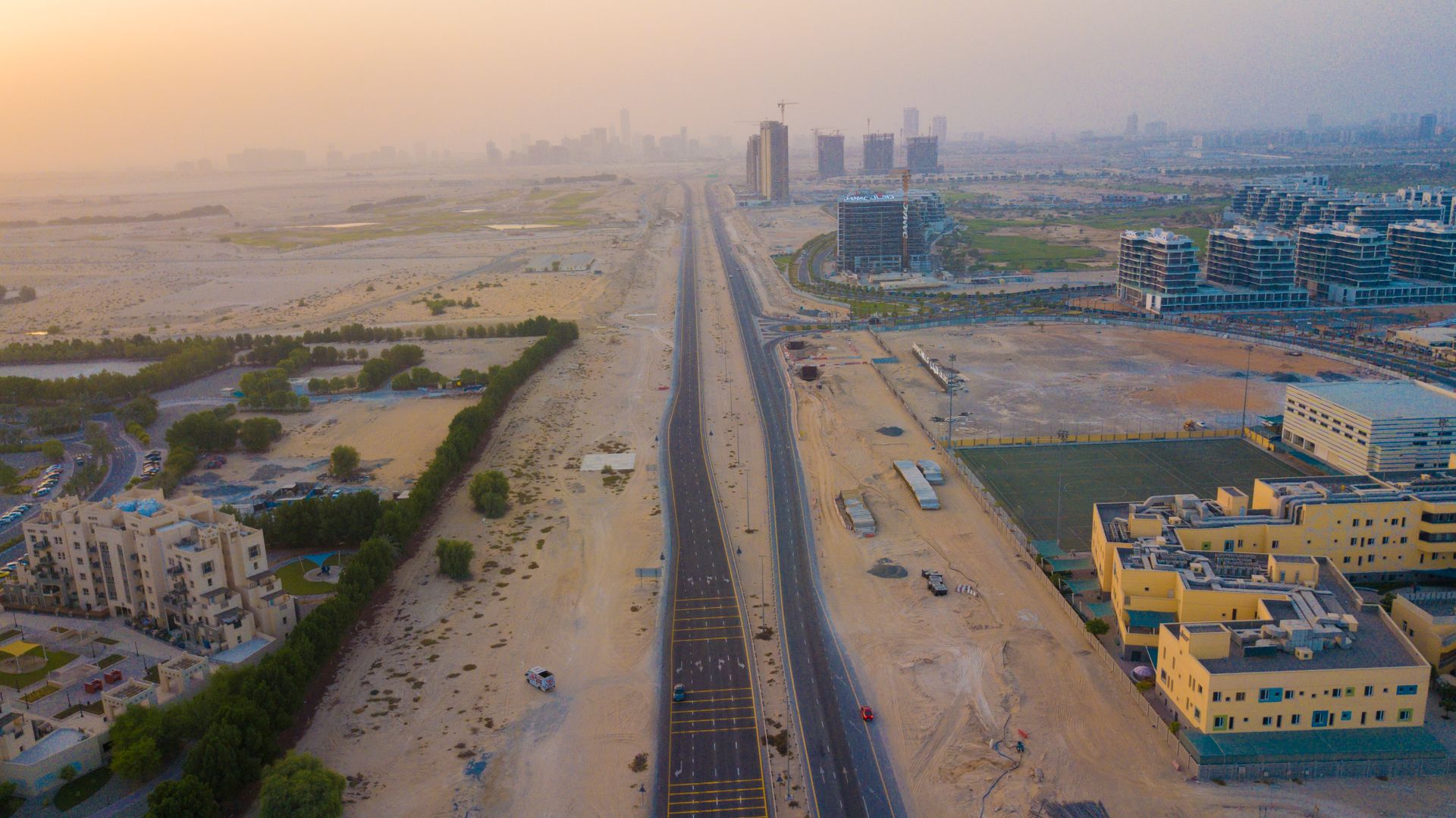 Aerial view showcasing Dubai's urban expansion with buildings and desert roads at sunset.