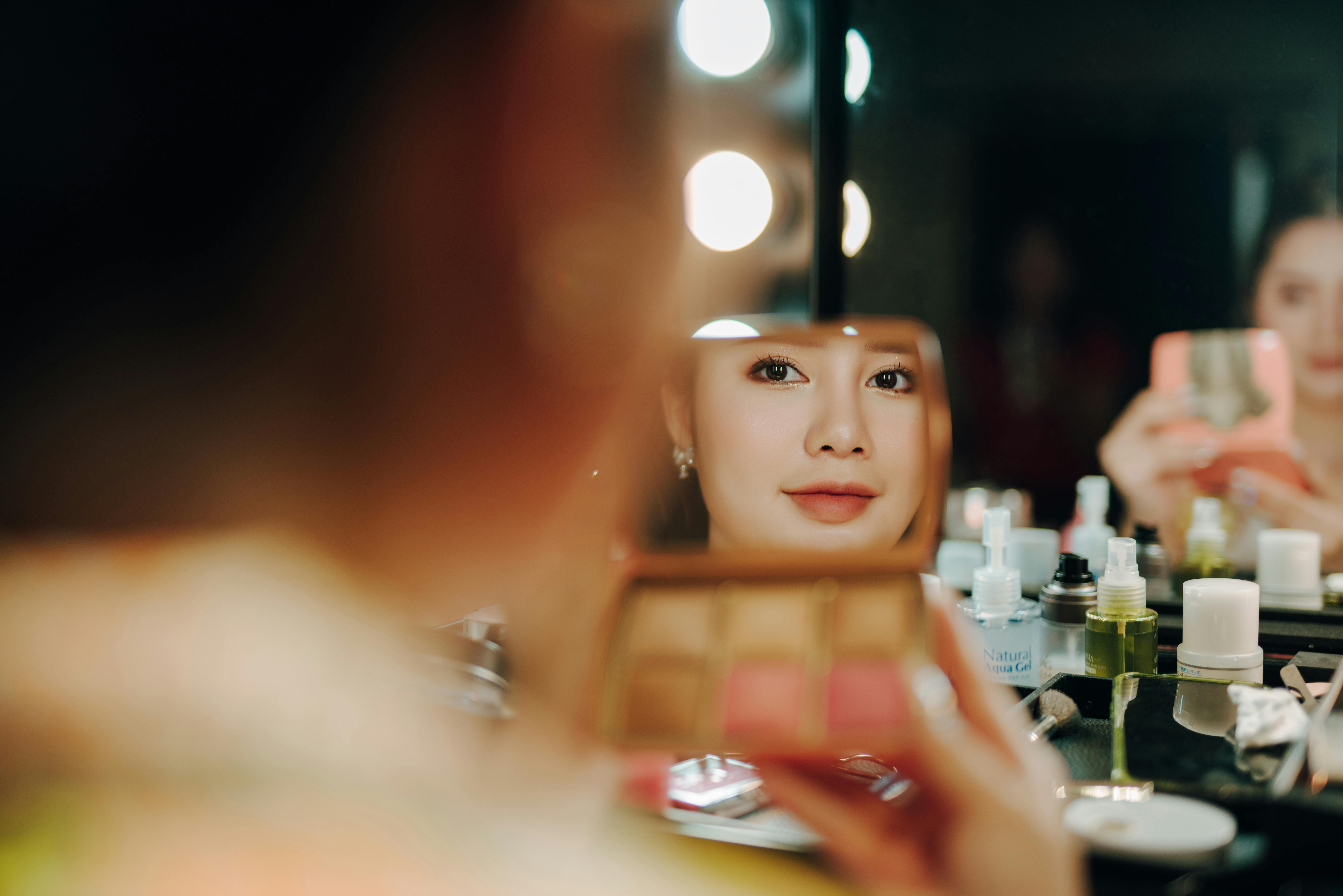 Woman smiling confidently at her reflection in a mirror with clean makeup products on her vanity - Clean makeup brands