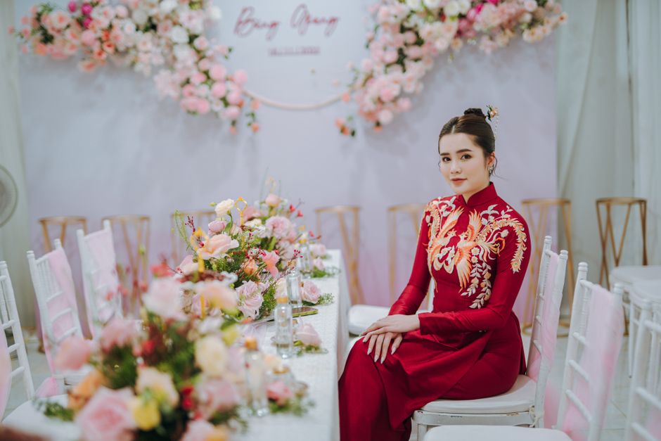 Elegant bride in a traditional red dress sitting at a beautifully decorated wedding table with floral accents.