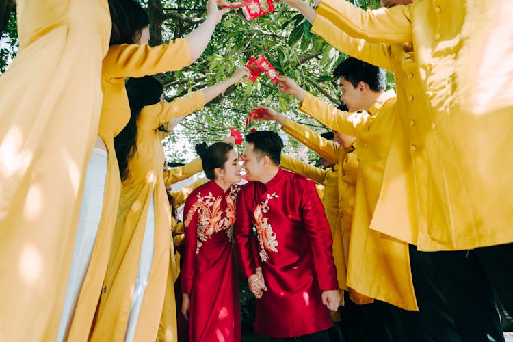 Wedding Couple Wearing Traditional Red Clothing And Row Of Guests Dressed In Yellow