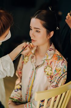 Woman getting makeup applied by artist in studio setting.
