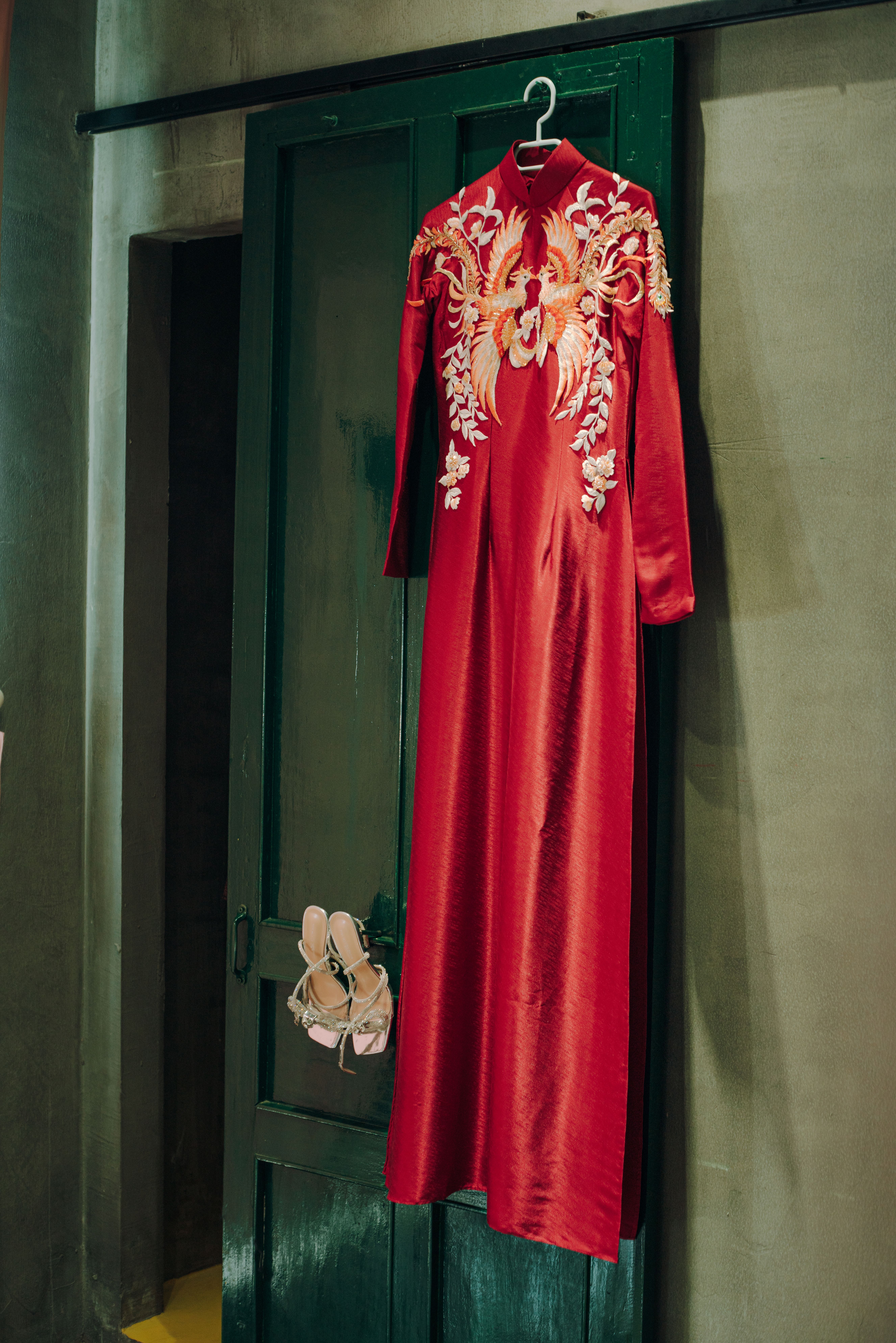 Long red silk dress with floral embroidery hanging on a wooden door.