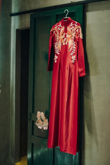 Long red silk dress with floral embroidery hanging on a wooden door.