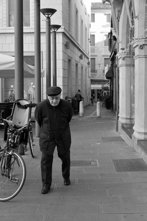 Free Black and white photo of an elderly man walking on a Treviso sidewalk, capturing urban life in Italy. Stock Photo