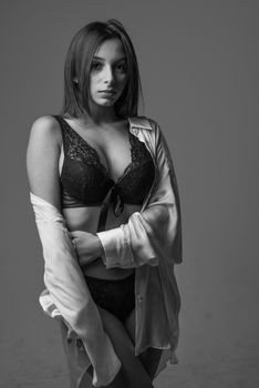 Black and white portrait of a woman in lingerie with a relaxed pose in a studio setting.