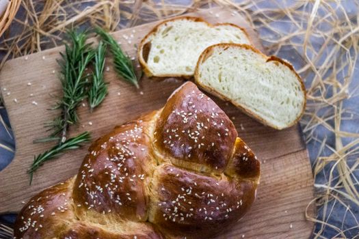 Close-up of freshly baked braided bread topped with sesame seeds, served on a wooden board with rosemary.