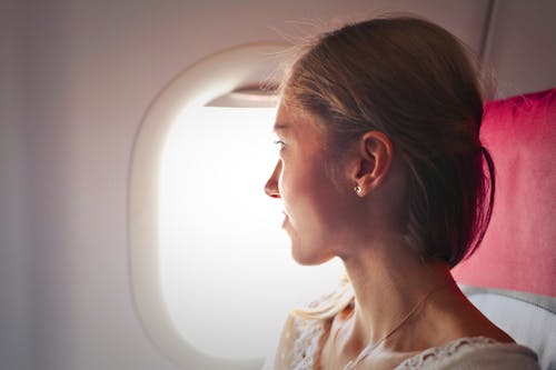 бесплатная Селективный фокус фото женщины, сидящей на стуле, глядя в окно на самолете Стоковое фото