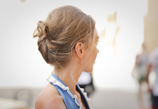 Side view of a woman with blonde hair styled in an updo, against a blurred indoor background.