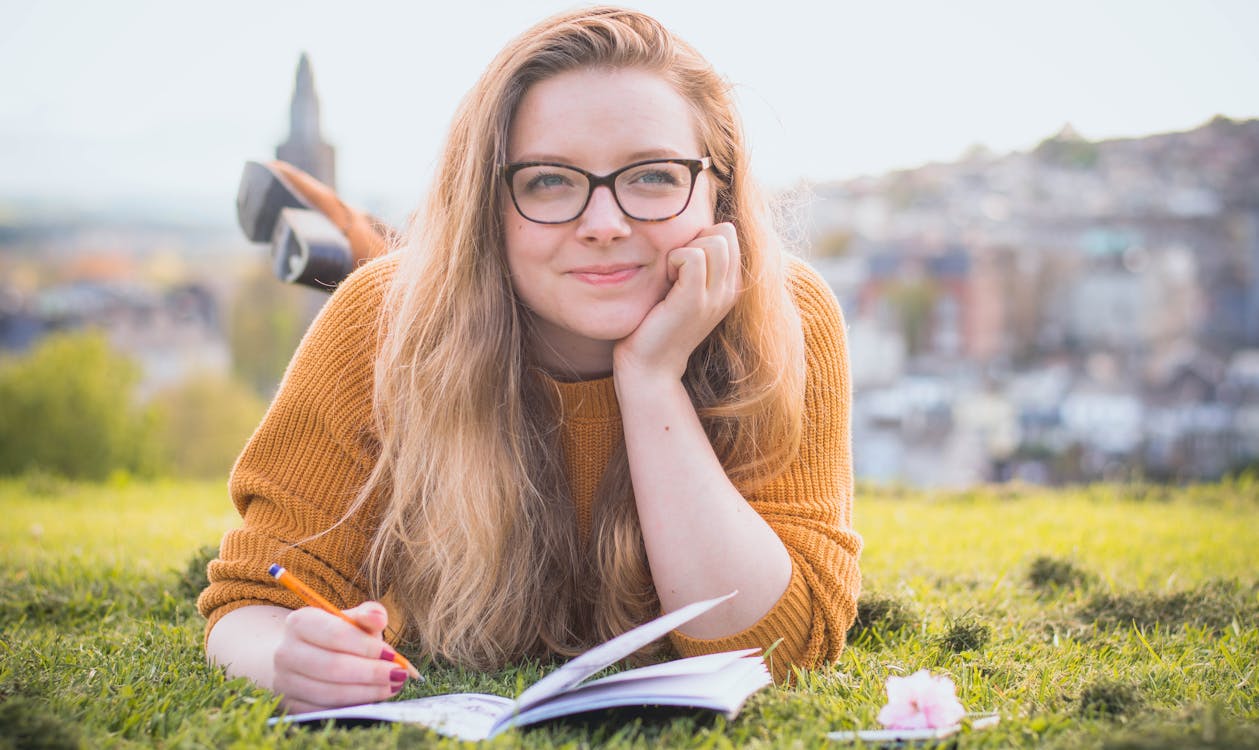 Woman Lying on Green Grass While Holding Pencil