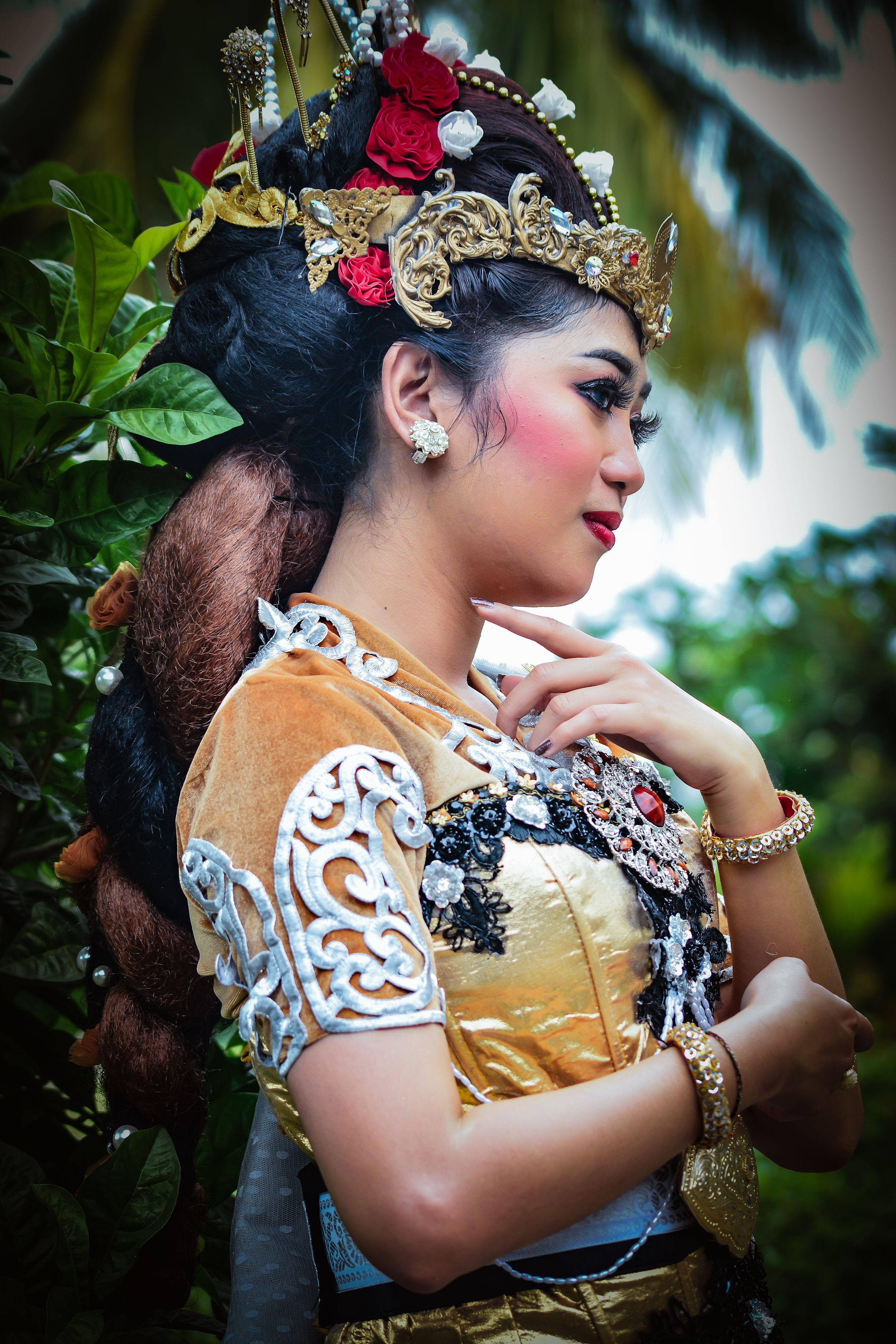 A woman in traditional Indonesian dress with ornate accessories in a tropical garden setting.