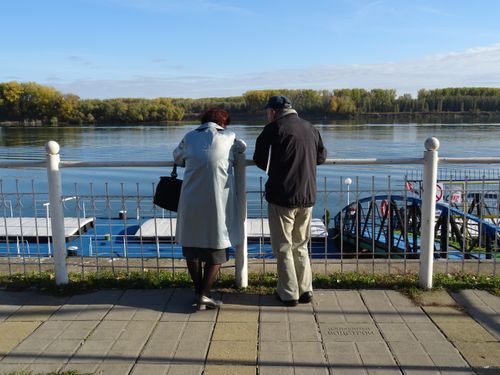 Free Senior couple standing by a river, enjoying the scenic view on a sunny day. Stock Photo