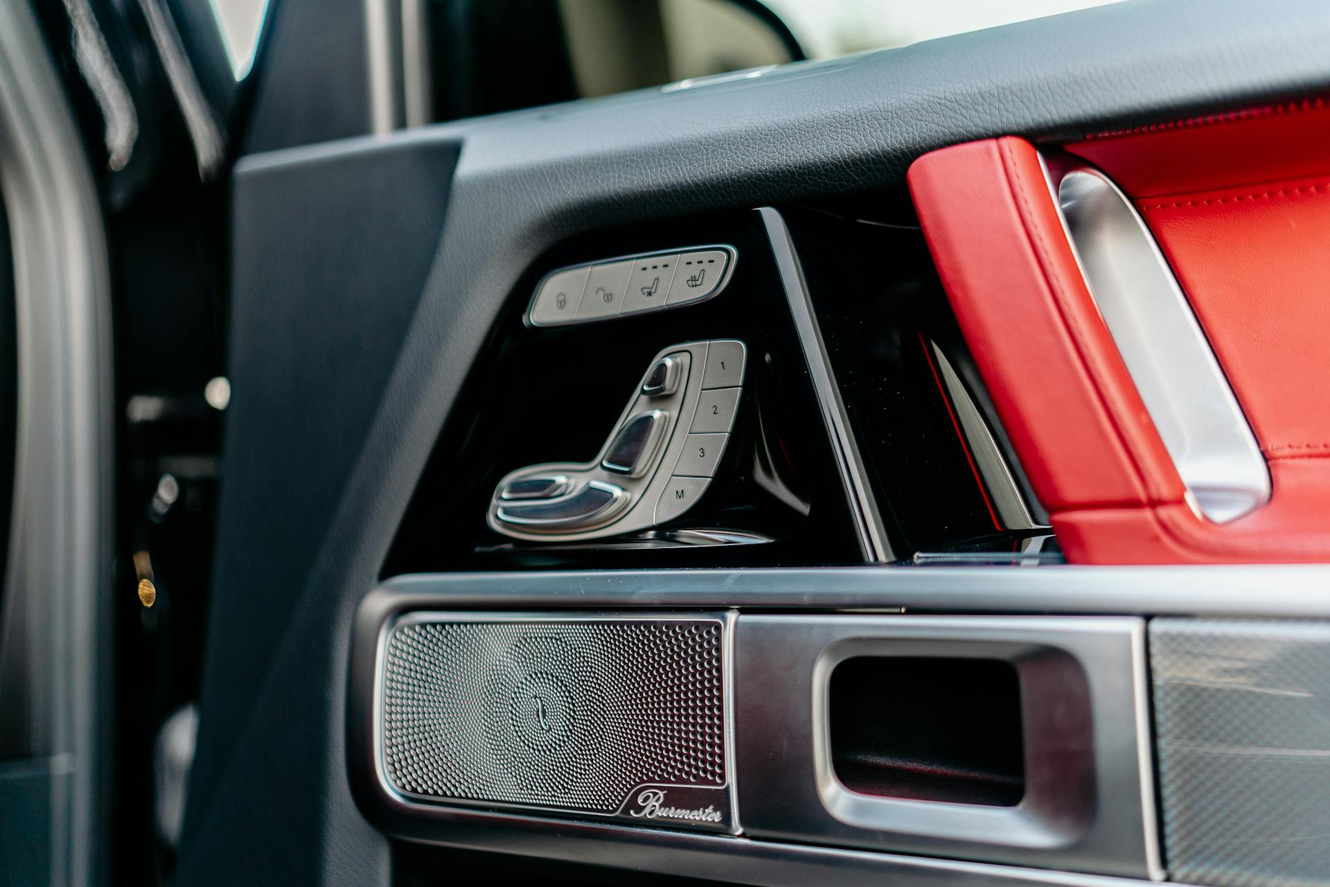 Close-up of modern luxury car door featuring red leather seats and metal trim controls.