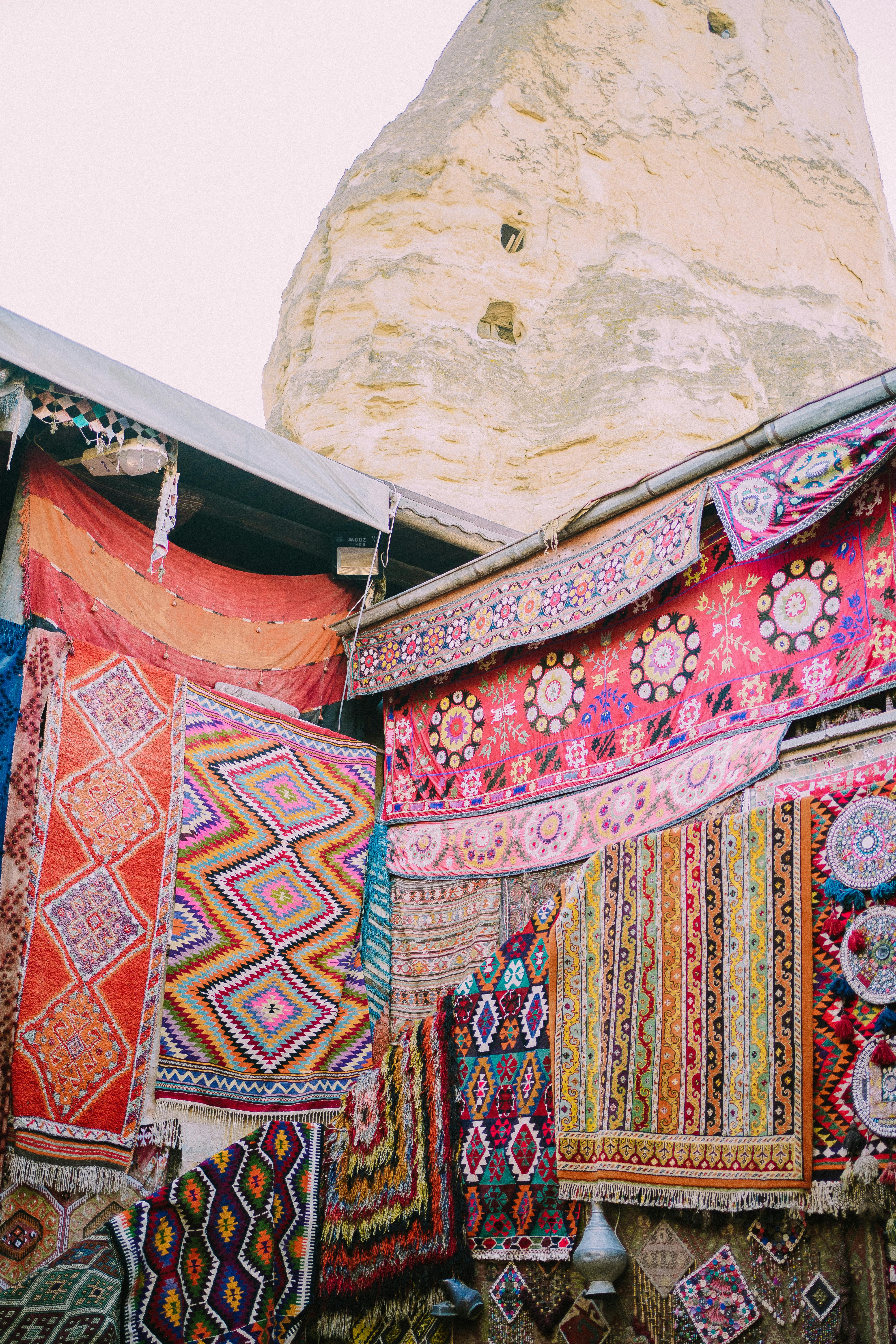 Vibrant handmade rugs showcased at a traditional Turkish market against a stone backdrop.