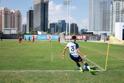 A young soccer player takes a corner kick on a sunny day in Dubai with skyscrapers in the background.