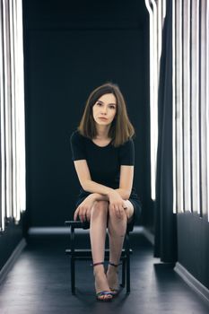 Stylish portrait of a woman in a black dress, seated elegantly under neon lights.
