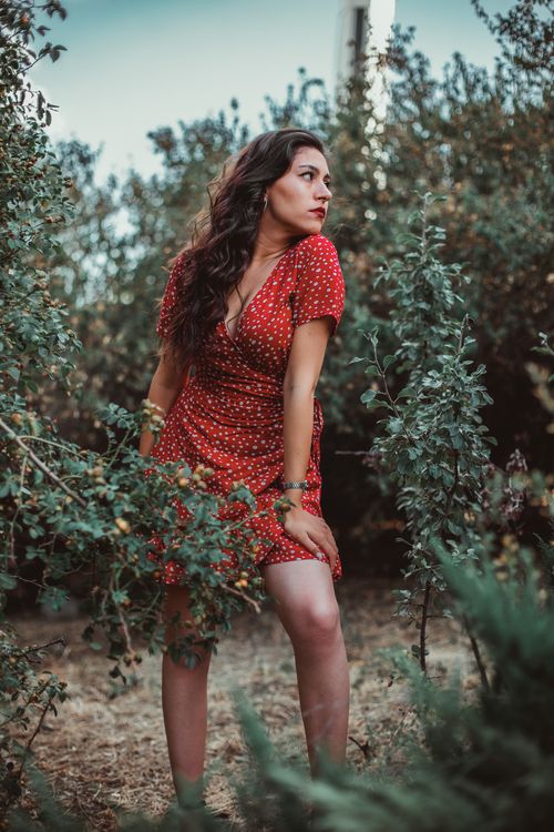 Free A woman in a red polka dot dress stands amidst lush garden greenery, embodying natural elegance. Stock Photo