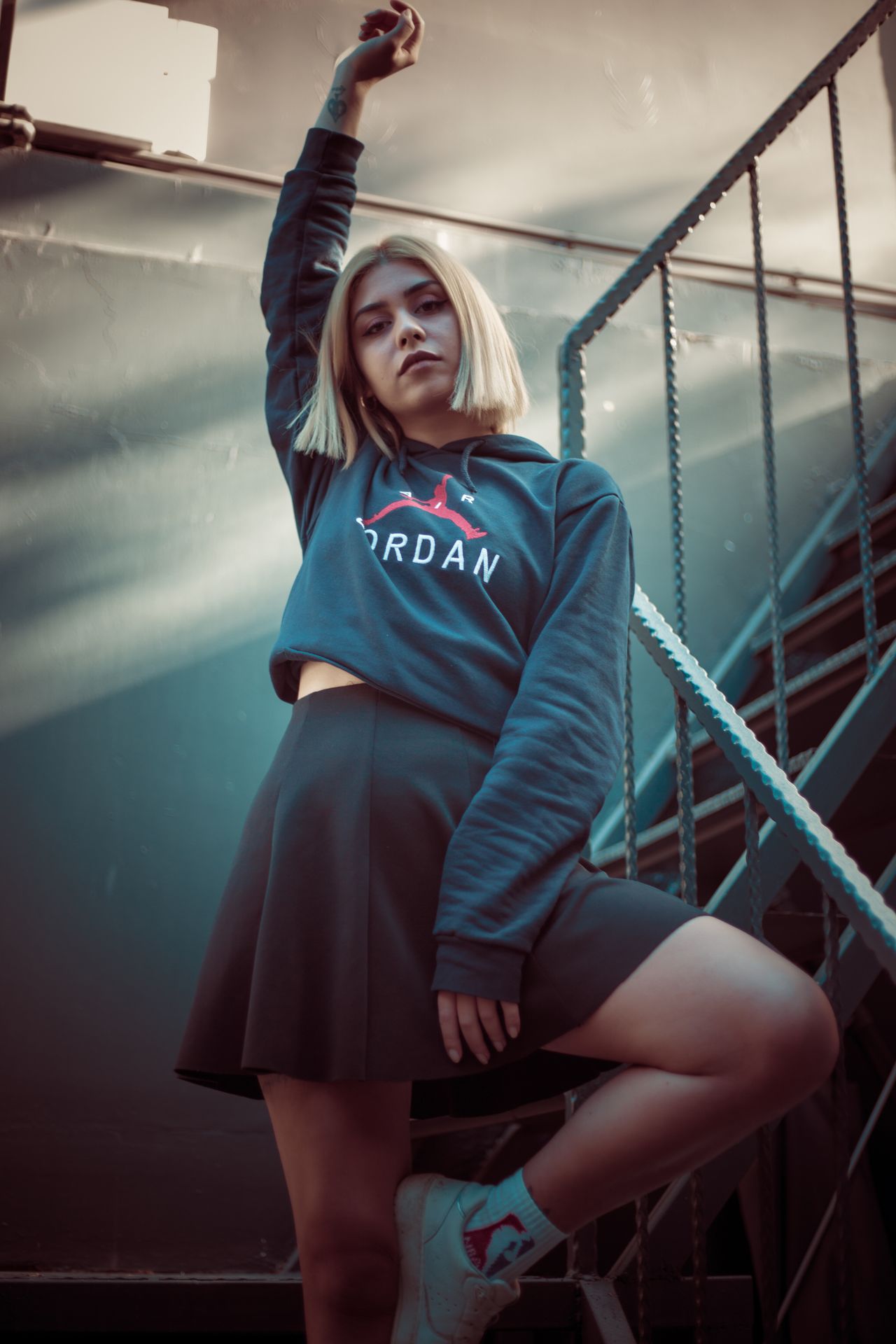 Woman in a navy hoodie and black skirt with sneakers on stairs