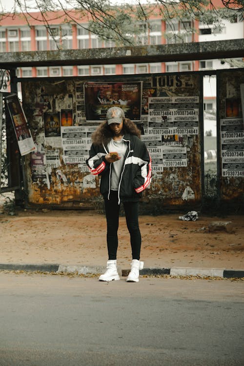 Young Black Woman Standing at the Bus Stop and Using Mobile Phone